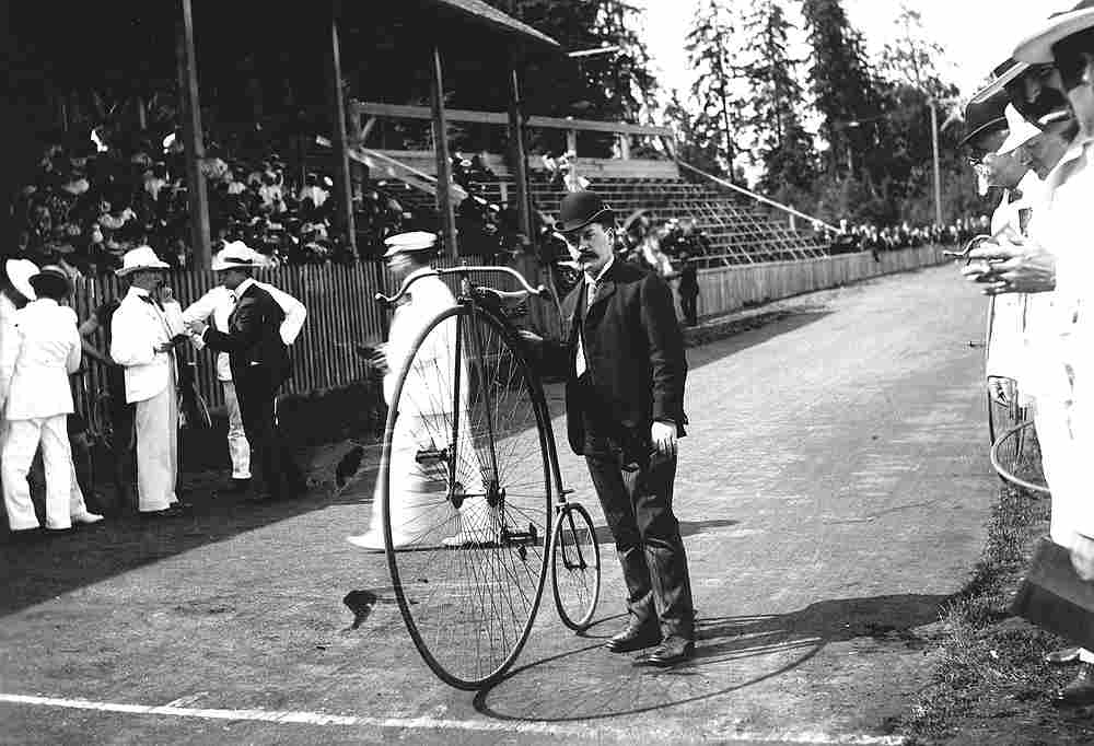 man-holding-a-high-wheel-bike-at-brockton-point-circa-1920
